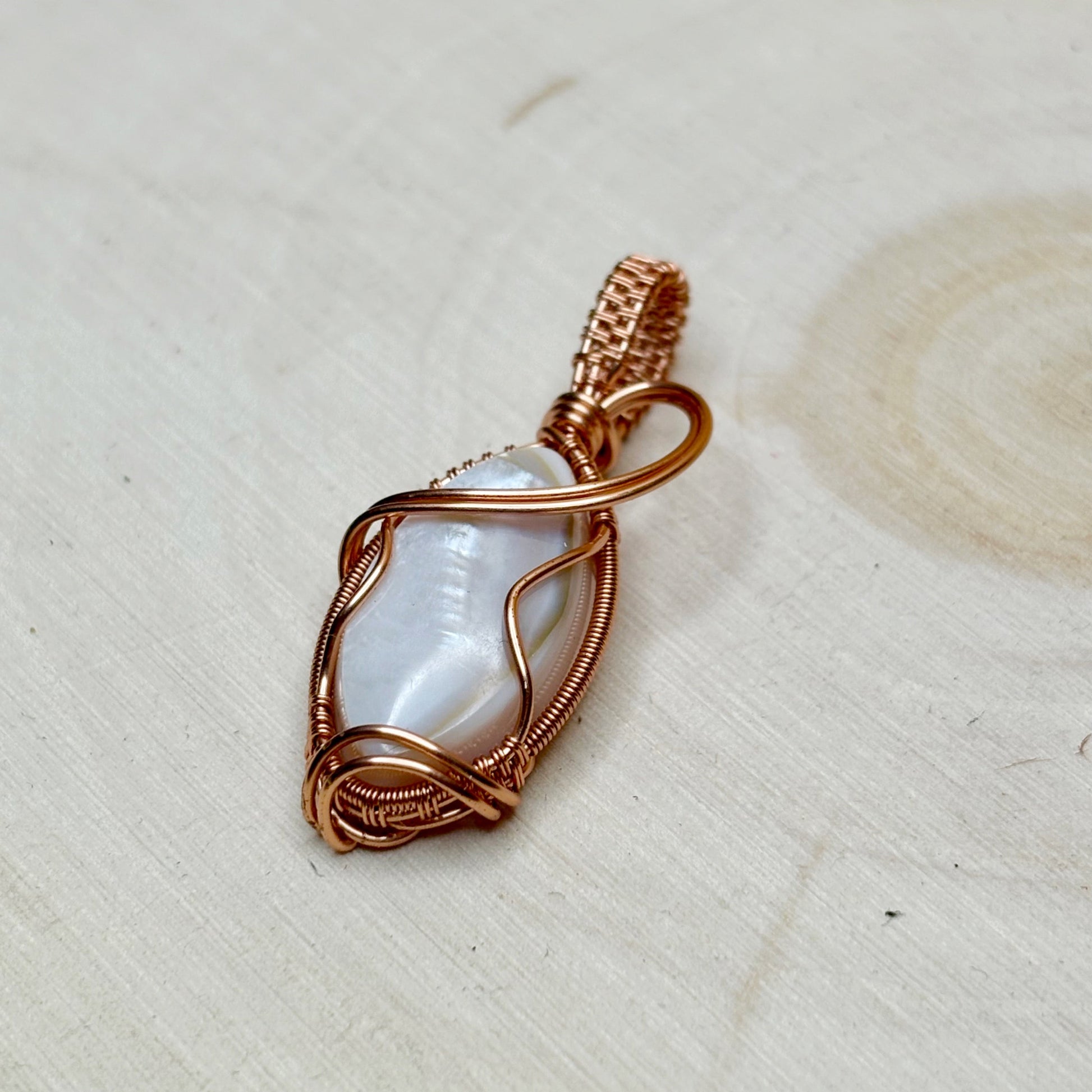 Copper-wrapped pendant with a central shell focal on a light wooden surface