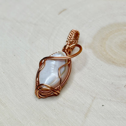 Copper-wrapped pendant with a central shell focal on a light wooden surface