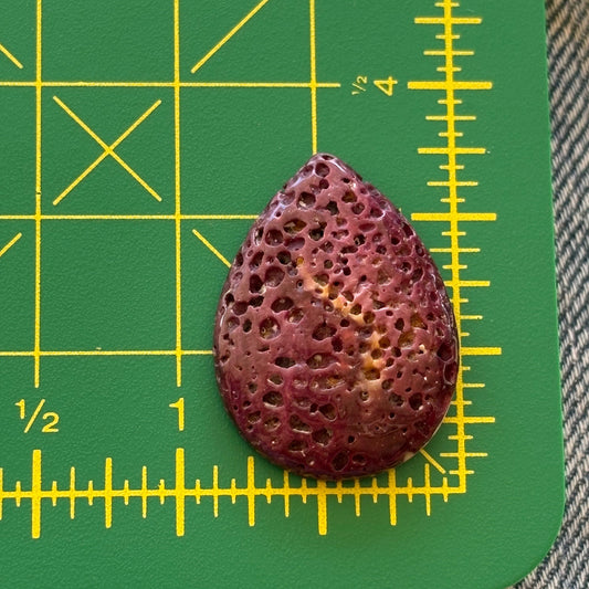 Teardrop-shaped purple stone on a green cutting mat with yellow measurements