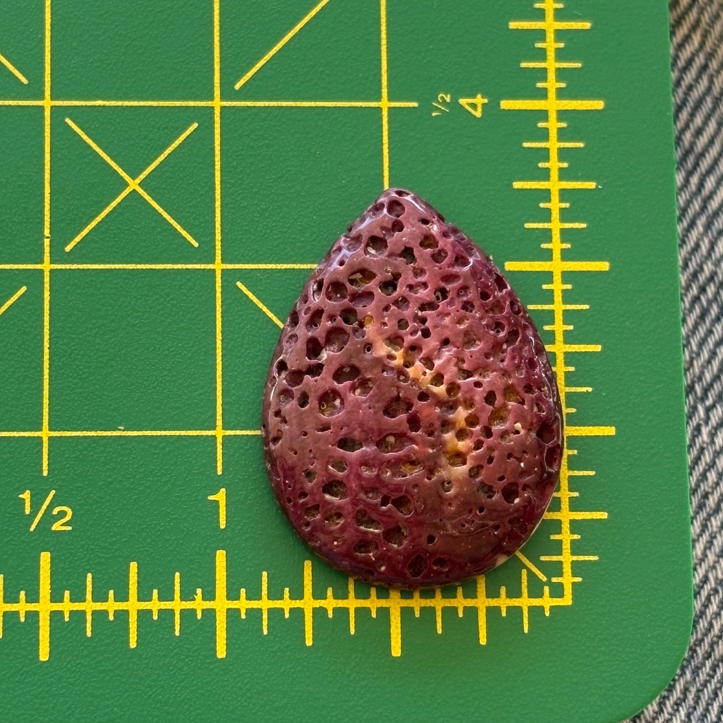 Teardrop-shaped purple stone on a green cutting mat with yellow measurements