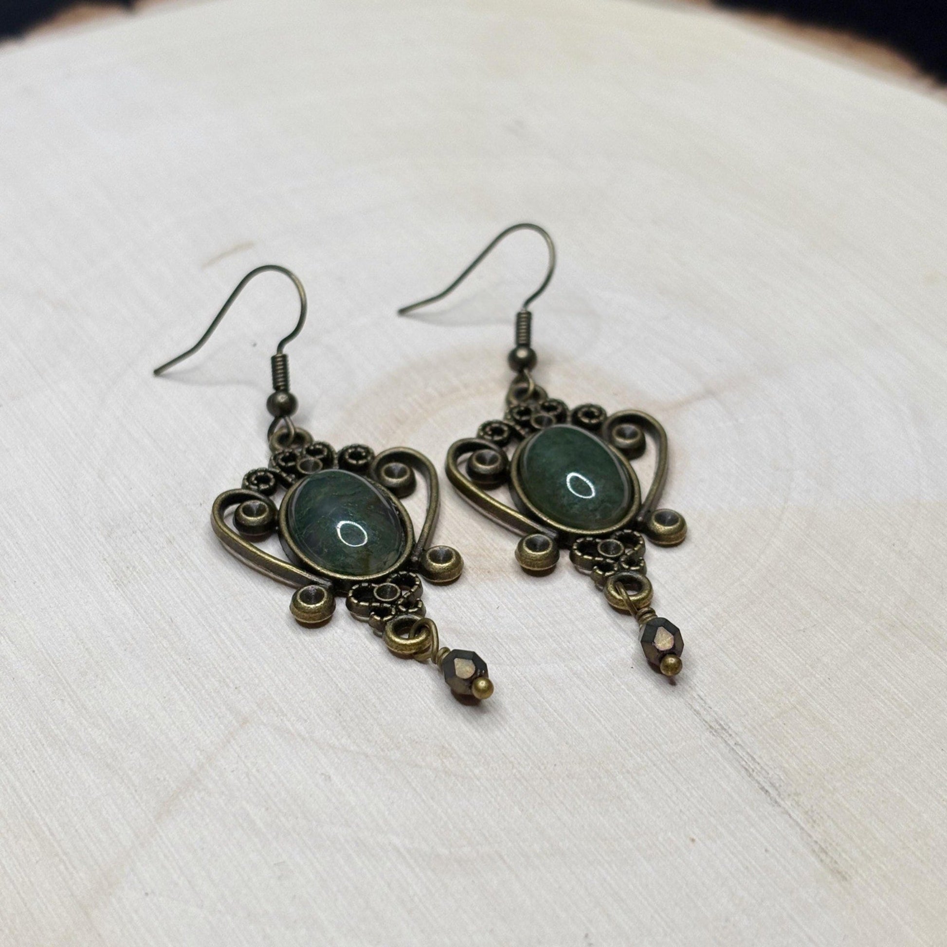 Pair of ornate earrings with green stones on a textured white surface