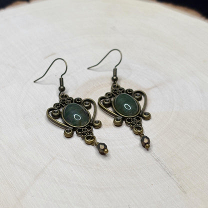 Pair of ornate earrings with green stones on a textured white surface