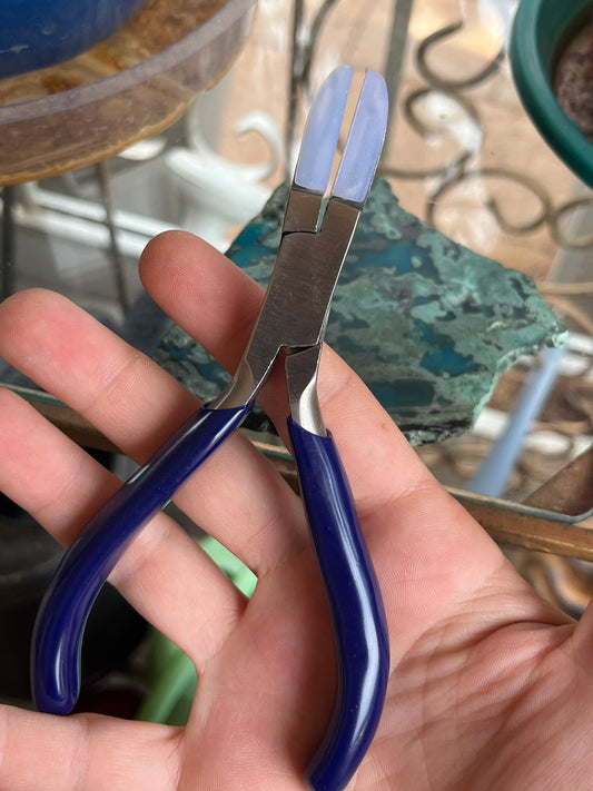 Hand holding a pair of pliers with blue handles outdoors-p