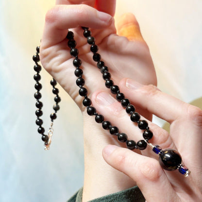 Black beaded rosary held by hands against a blurred background