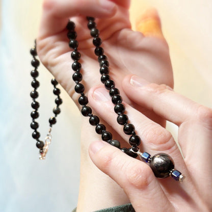 Close-up of hands holding a black beaded necklace with a blurred background