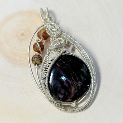 Silver wire-wrapped pendant with a dark stone and smaller brown stones on a light wooden surface