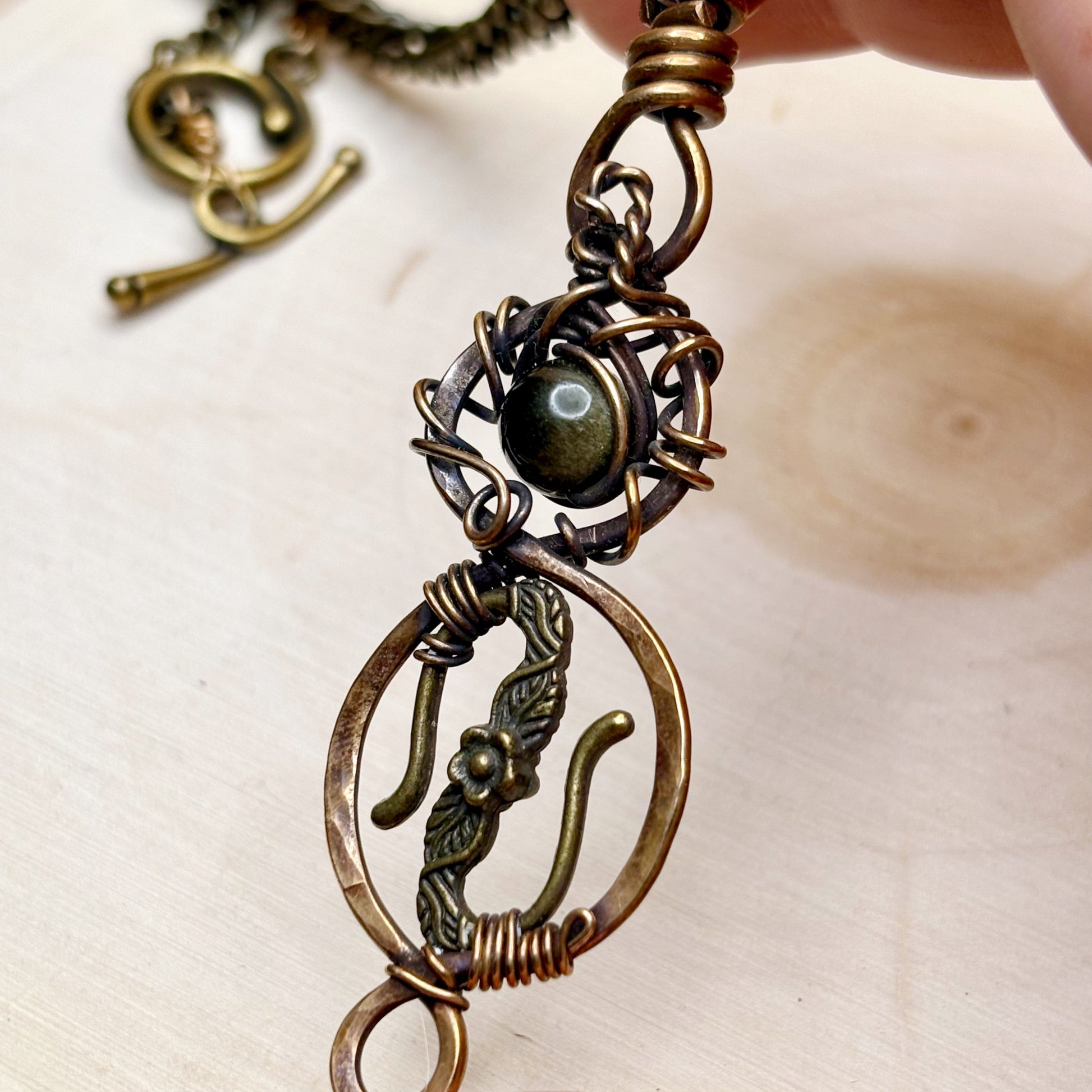 Close-up of a detailed bronze pendant with a central gold gemstone on a light background.
