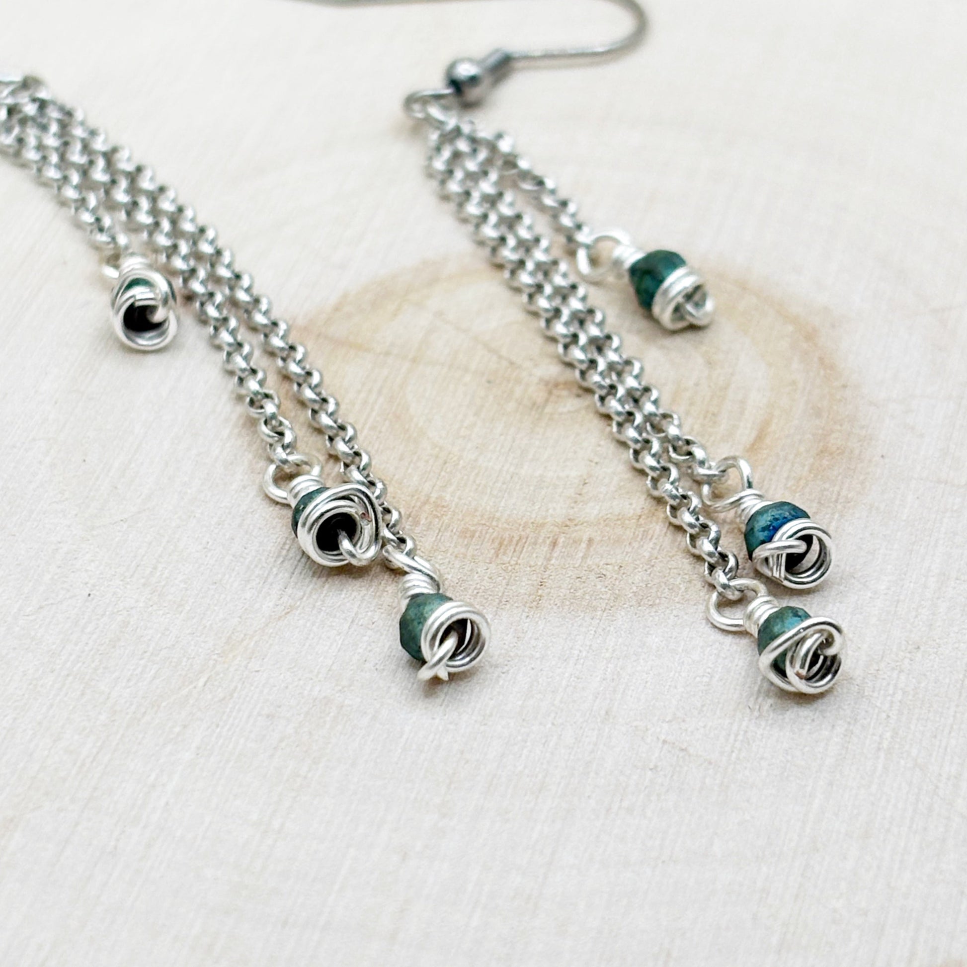 Silver chain earrings with green beads on a light wooden surface