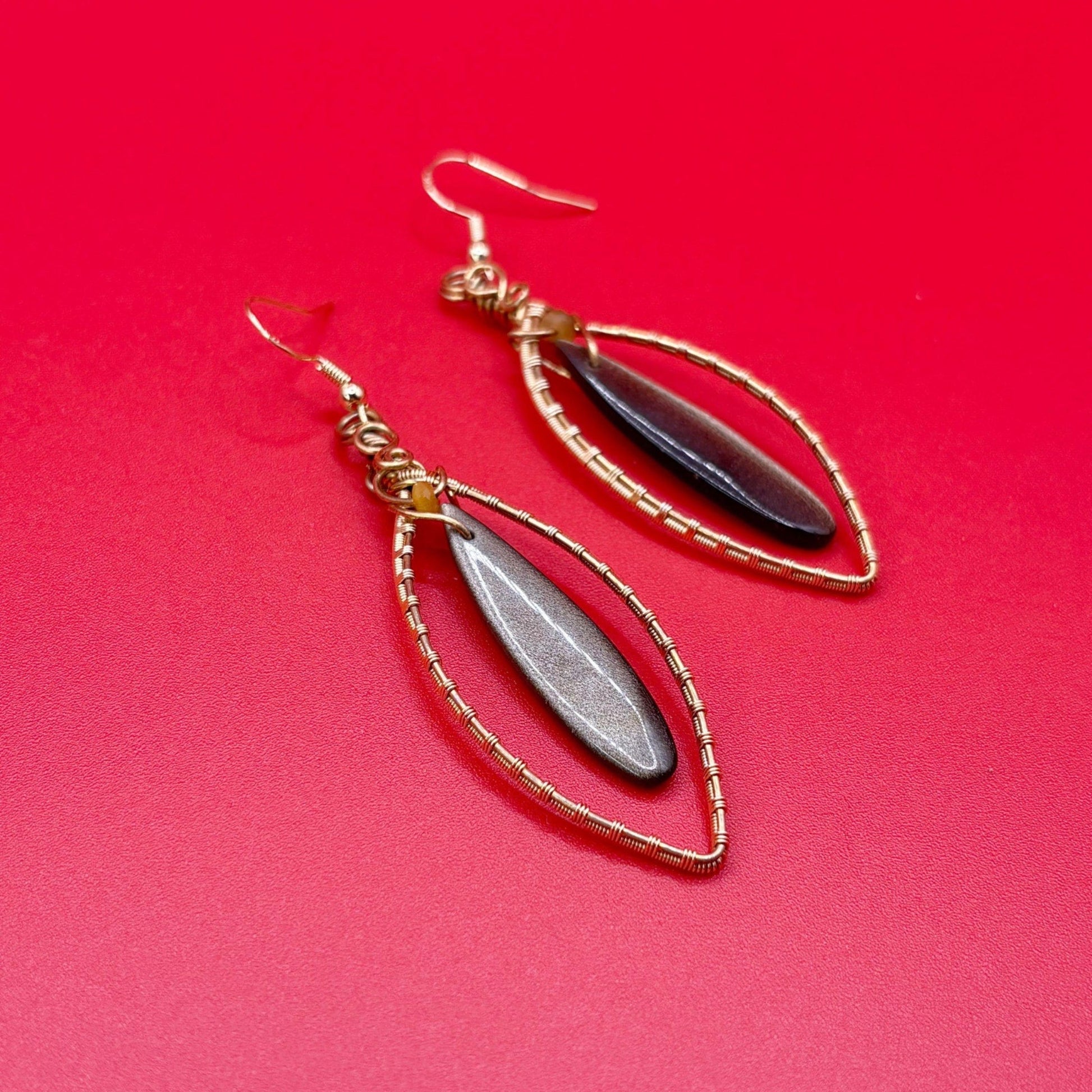 Pair of earrings with gold wire wrapping and black and gold stones on a red background