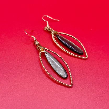 Pair of earrings with gold wire wrapping and black and gold stones on a red background