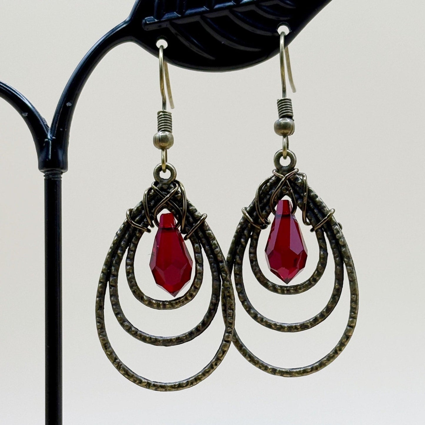 Pair of earrings with red teardrop stones on a black stand.
