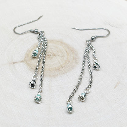 Pair of silver chain earrings with small circular charms on a light background
