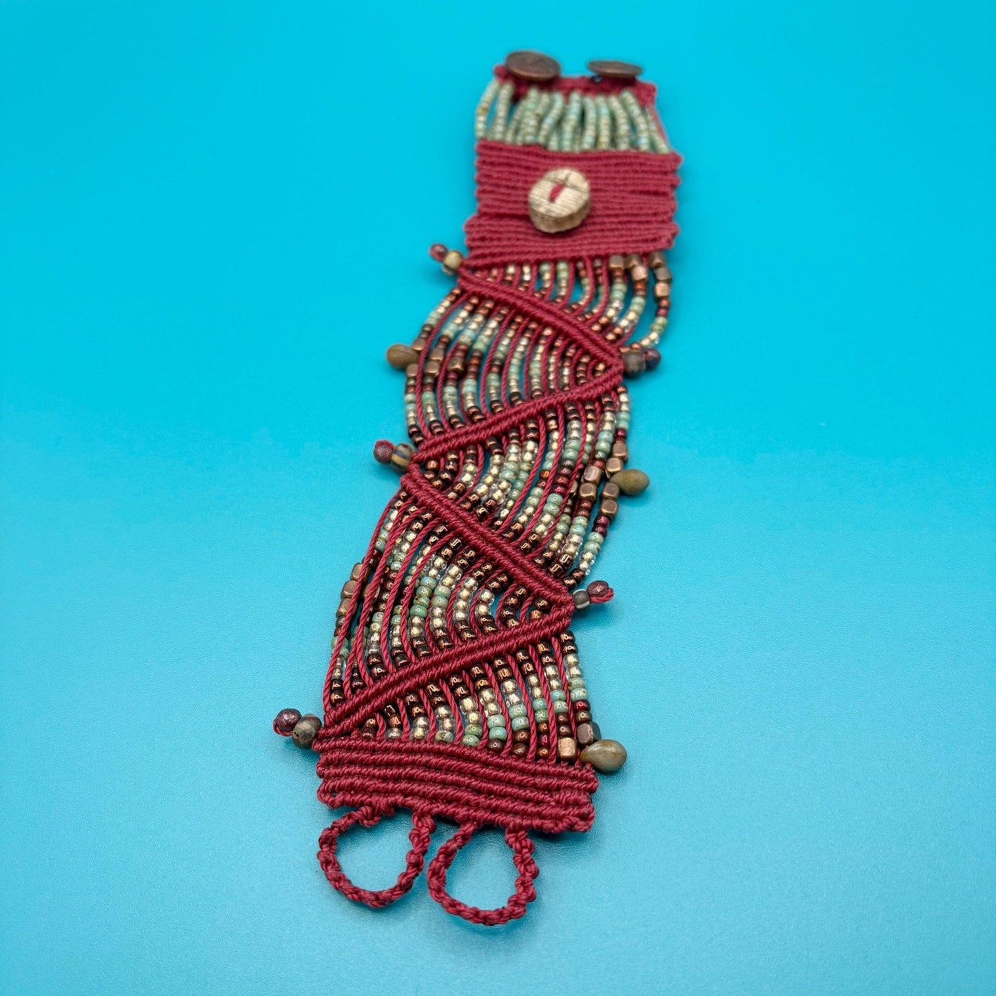 Red and copper macrame bracelet on a blue background
