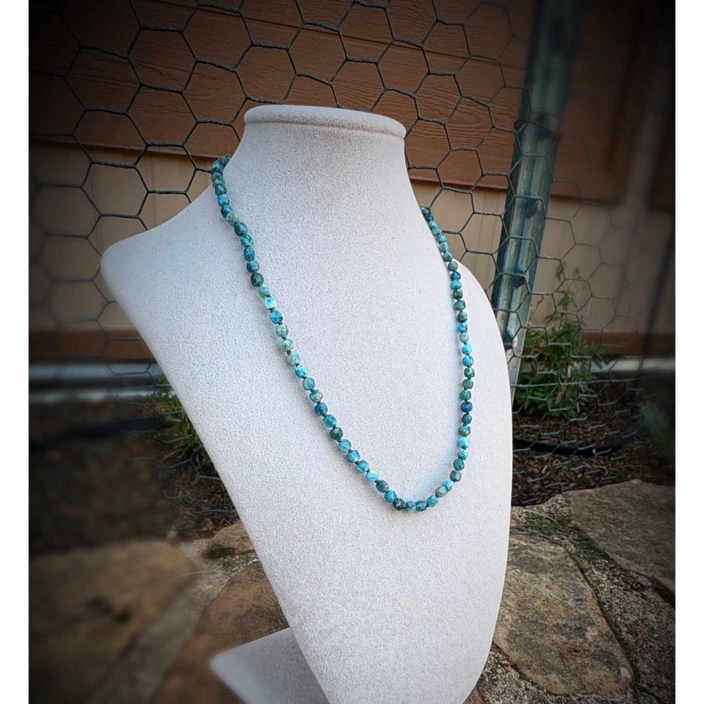 dark blue beaded necklace on a white mannequin bust against a rustic background.