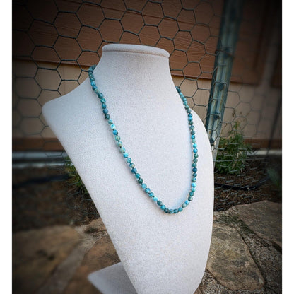 dark blue beaded necklace on a white mannequin bust against a rustic background.