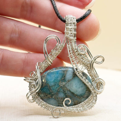 Silver wire-wrapped pendant with a blue stone held in a hand against a beige background
