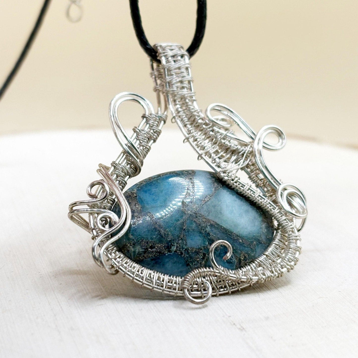 Silver-wrapped pendant with a blue stone on a white surface