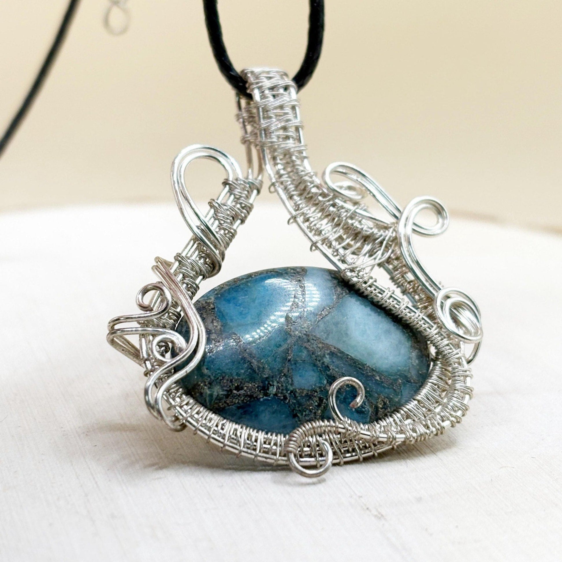 Silver-wrapped pendant with a blue stone on a white surface