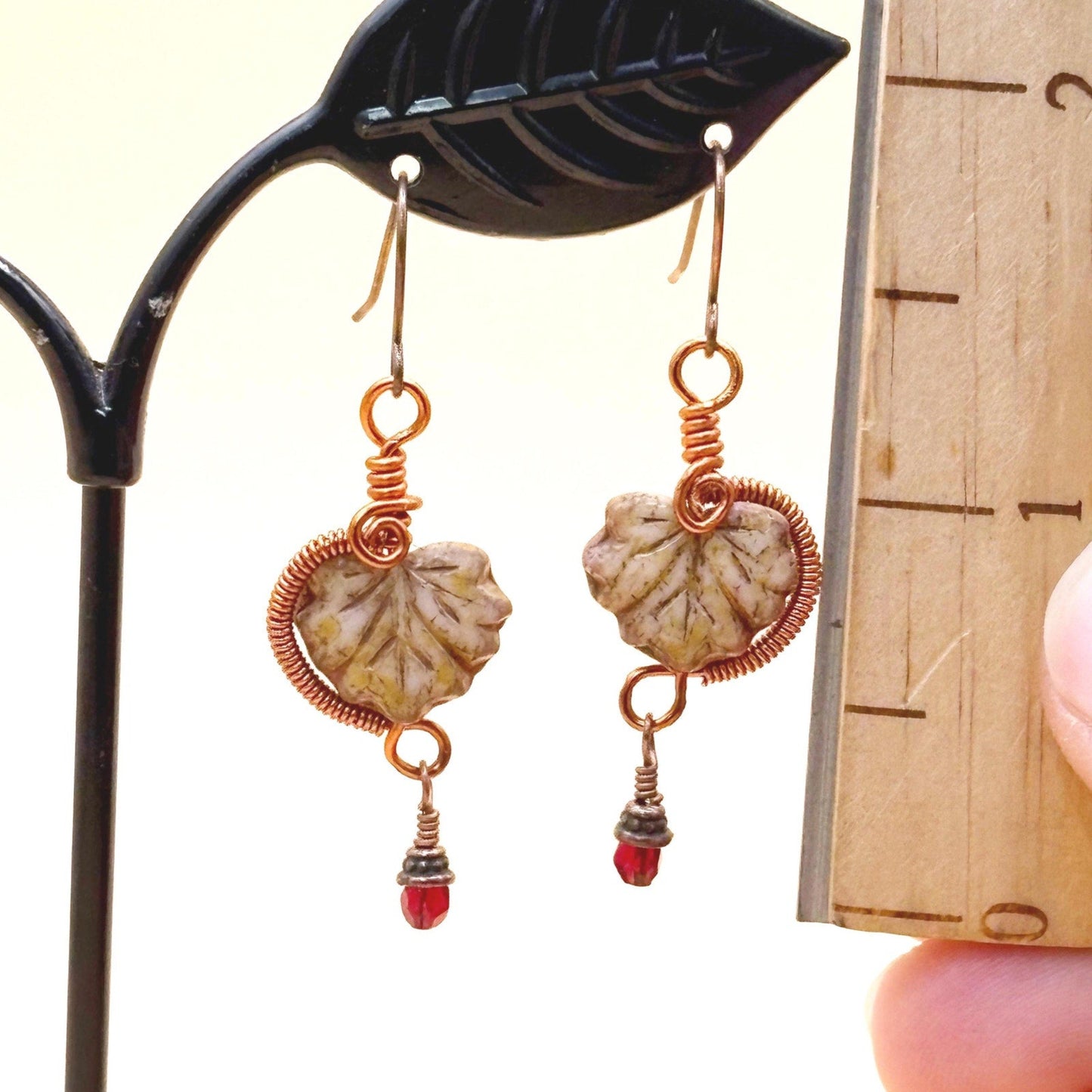Pair of earrings with glass leaves and red bead details on a stand.