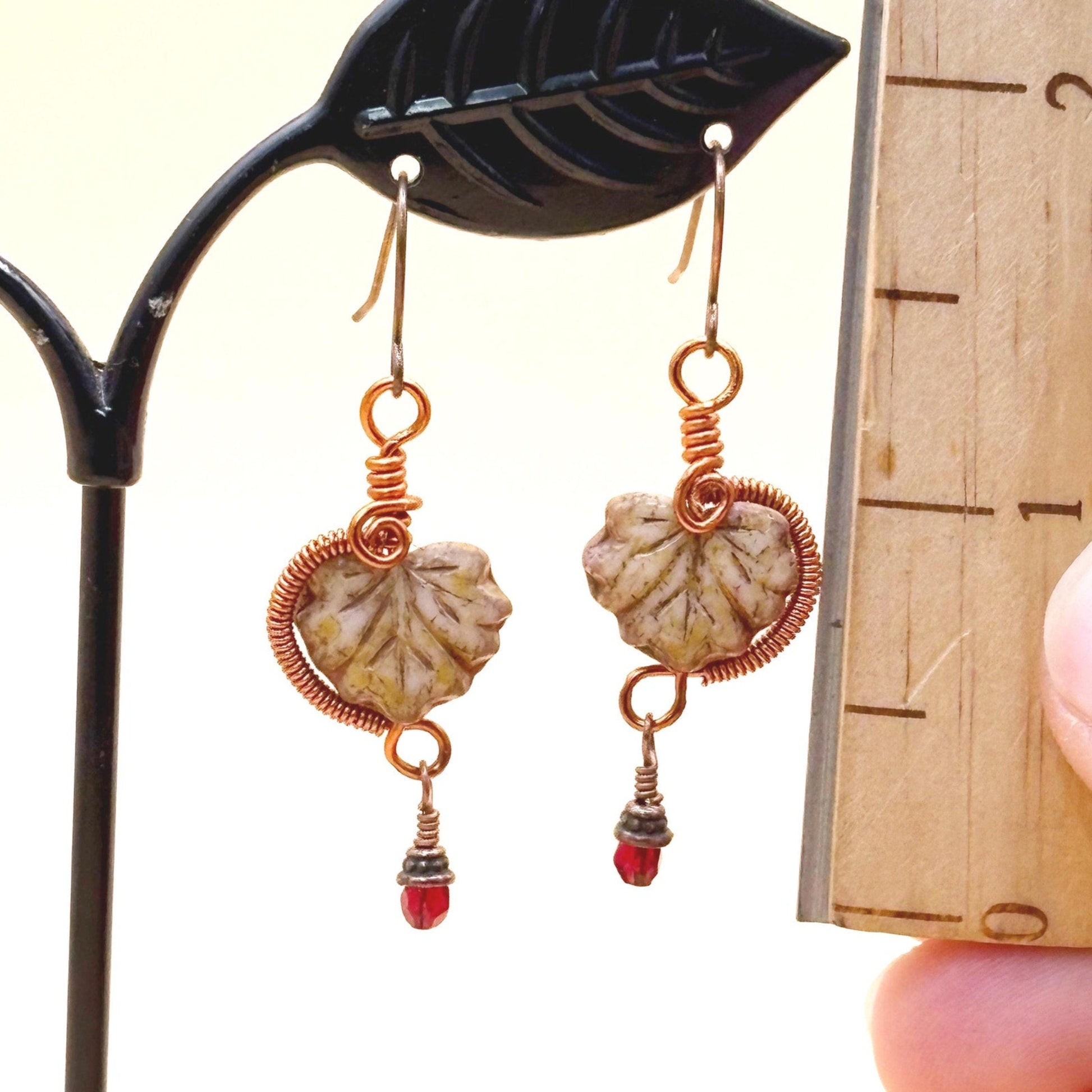 Pair of earrings with glass leaves and red bead details on a stand.
