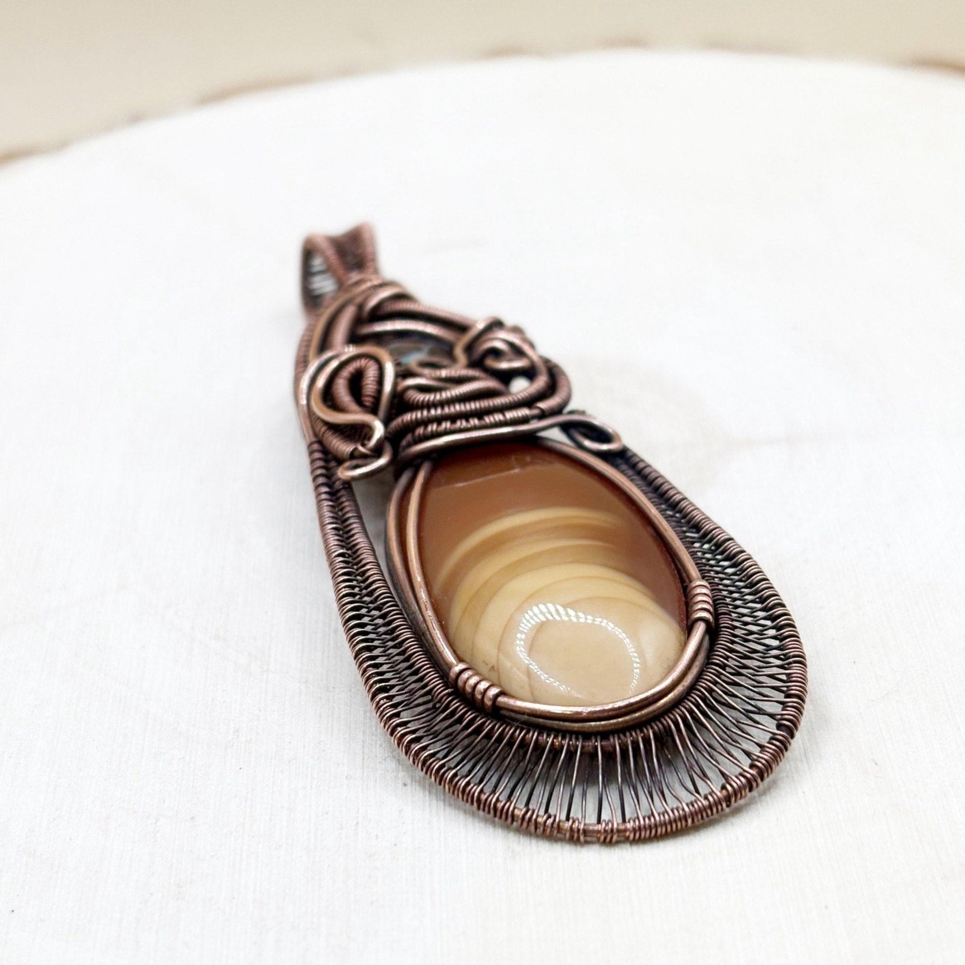 Copper-wrapped pendant with a central stone on a white background