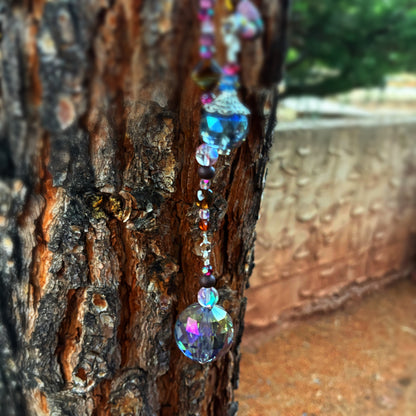 Decorative beaded string with colorful beads hanging on a tree trunk.