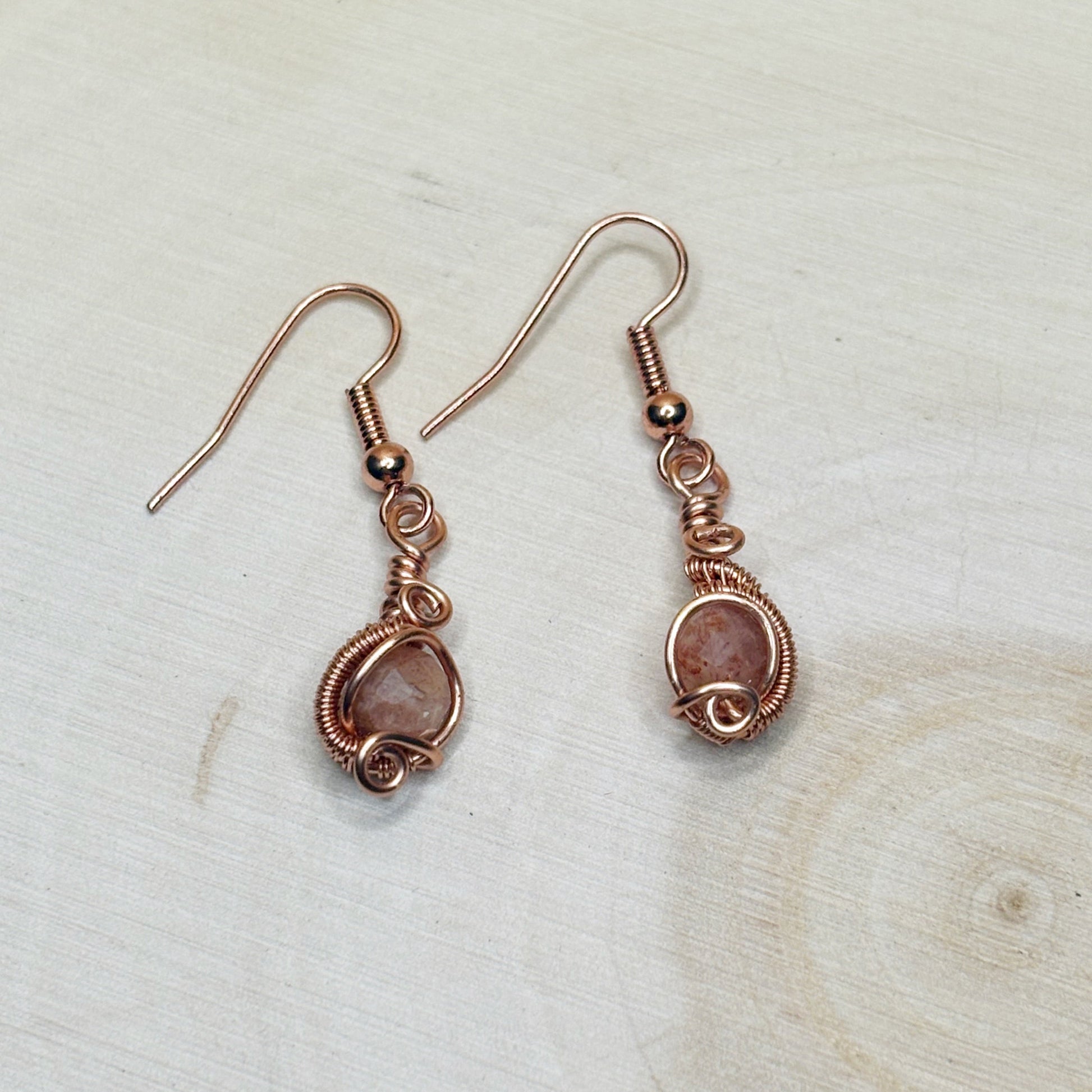Pair of copper wire-wrapped earrings with orange stones on a light wooden surface