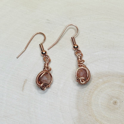 Pair of copper wire-wrapped earrings with orange stones on a light wooden surface