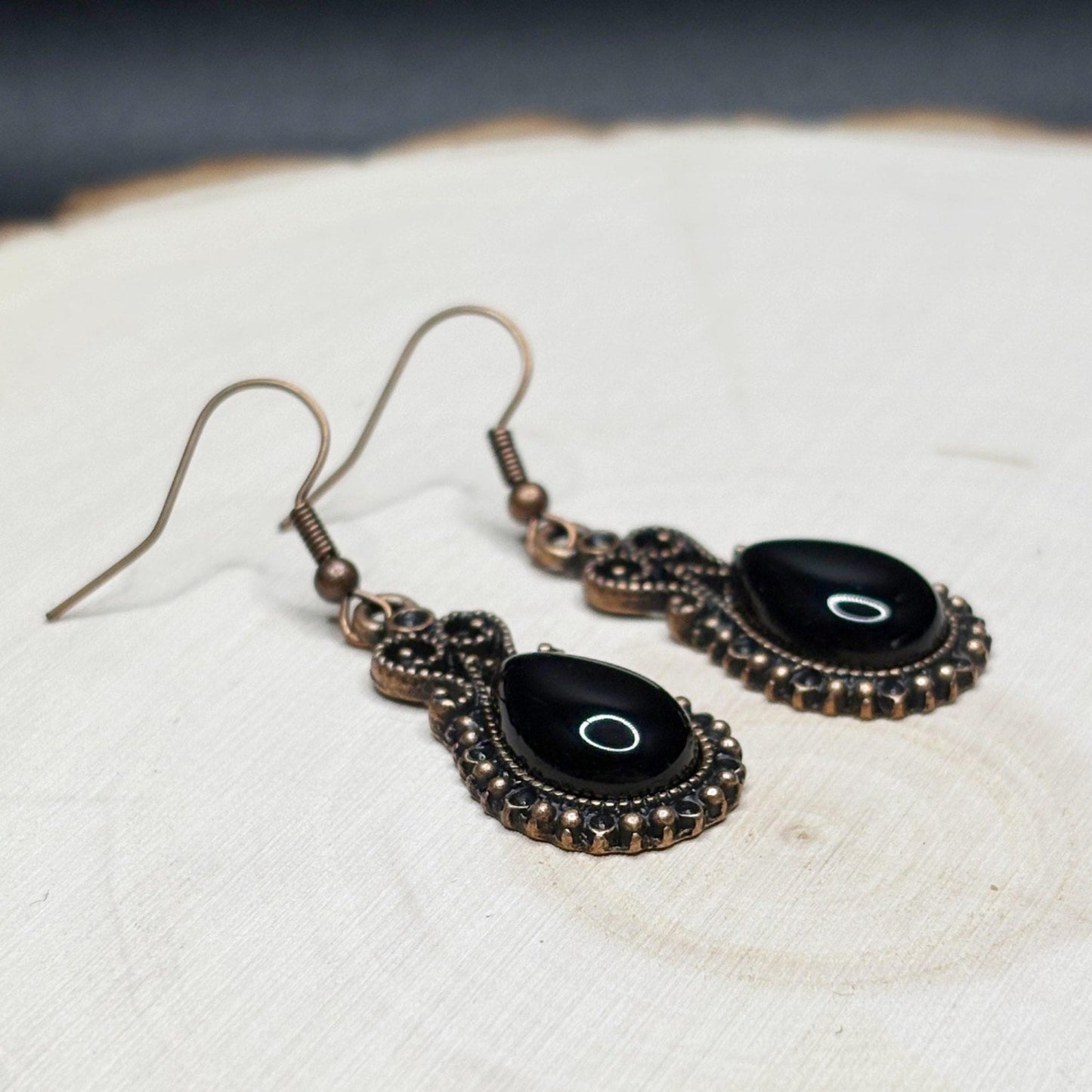 Pair of black and copper earrings on a textured white surface
