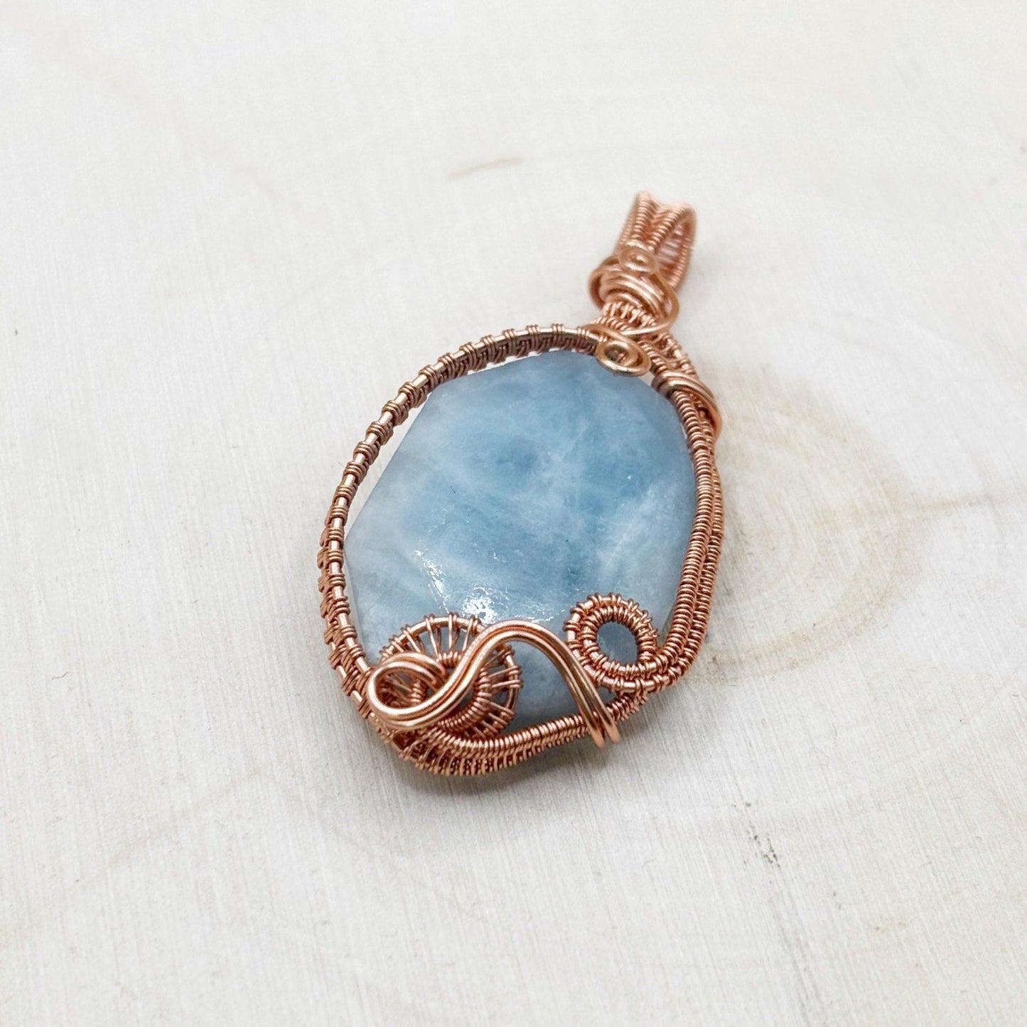 Blue stone pendant with copper wire wrapping on a white background