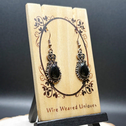 Pair of black teardrop earrings on a wooden display card with 'Wire Weaved Uniques' branding.