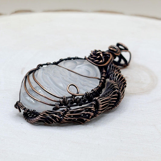 Decorative copper pendant with a central stone that is carved into the shape of an owl on a white wood background-p