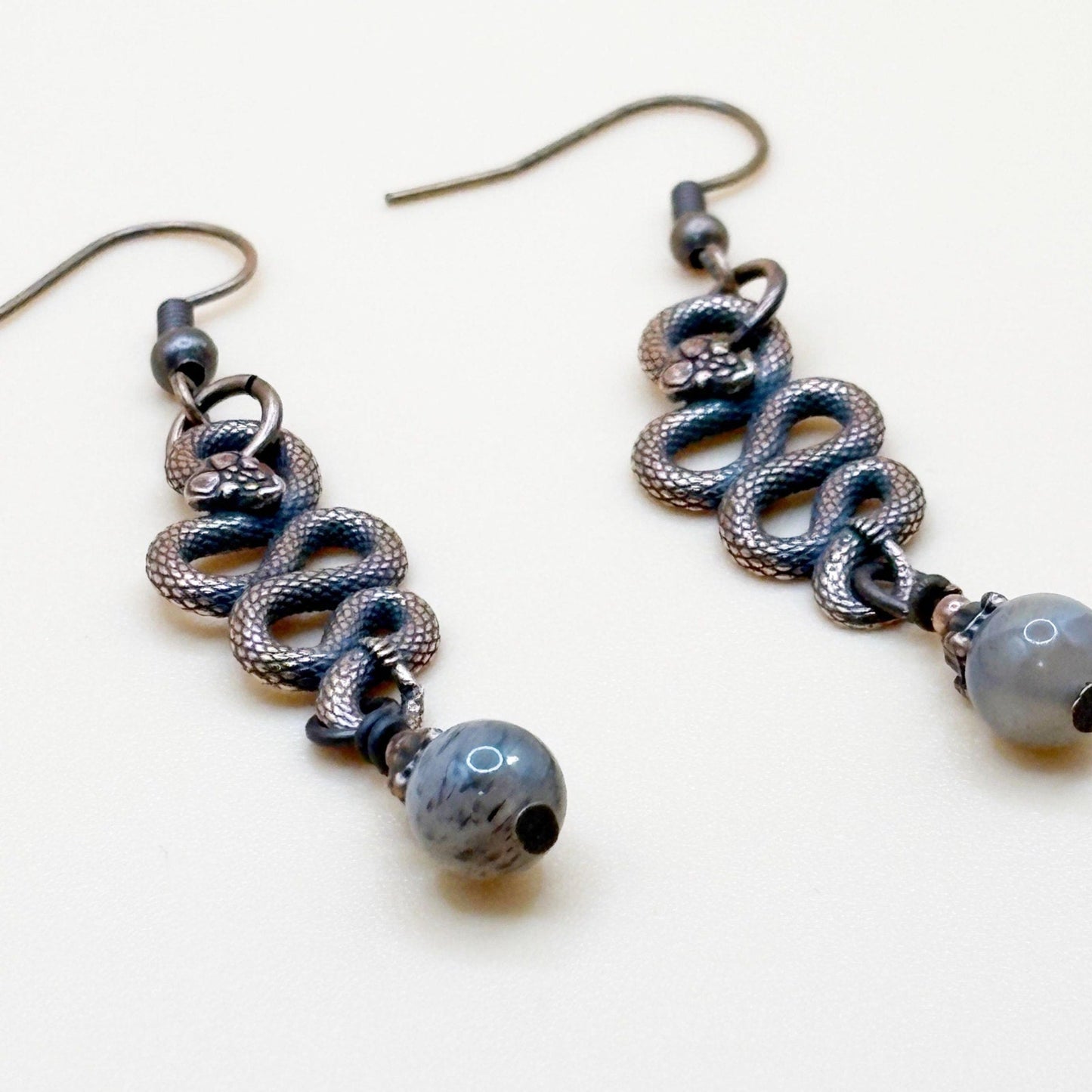 Pair of copper tone snake shape earrings with beads that dangle on a white background