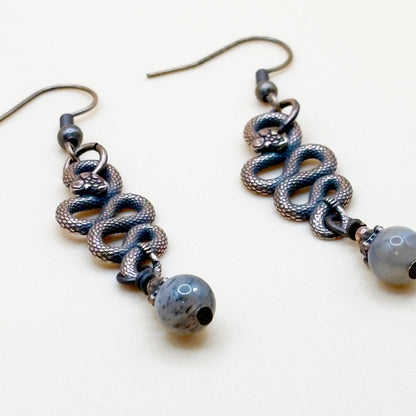 Pair of copper tone snake shape earrings with beads that dangle on a white background