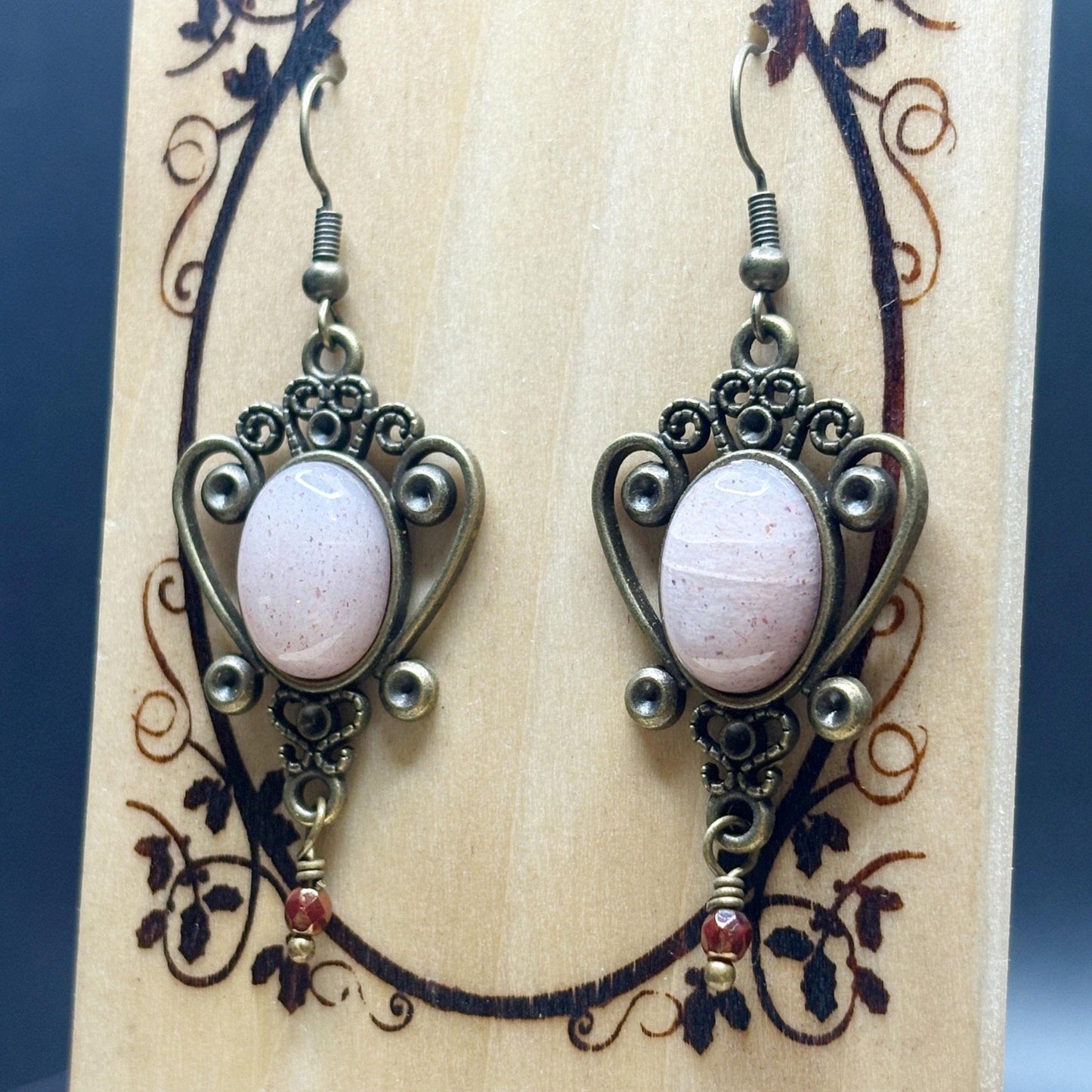 Pair of ornate earrings with pink stones on a decorative wooden stand.