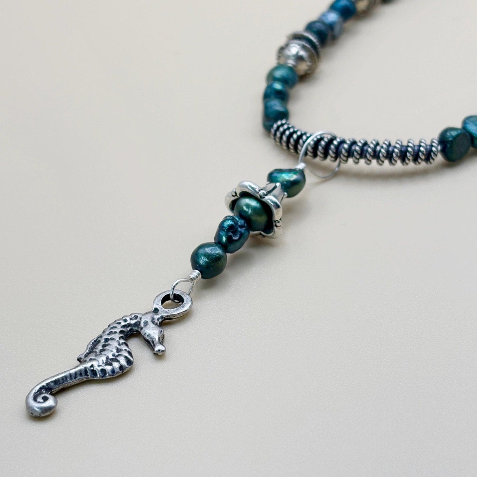 Necklace with green beads and a silver seahorse charm on a light background