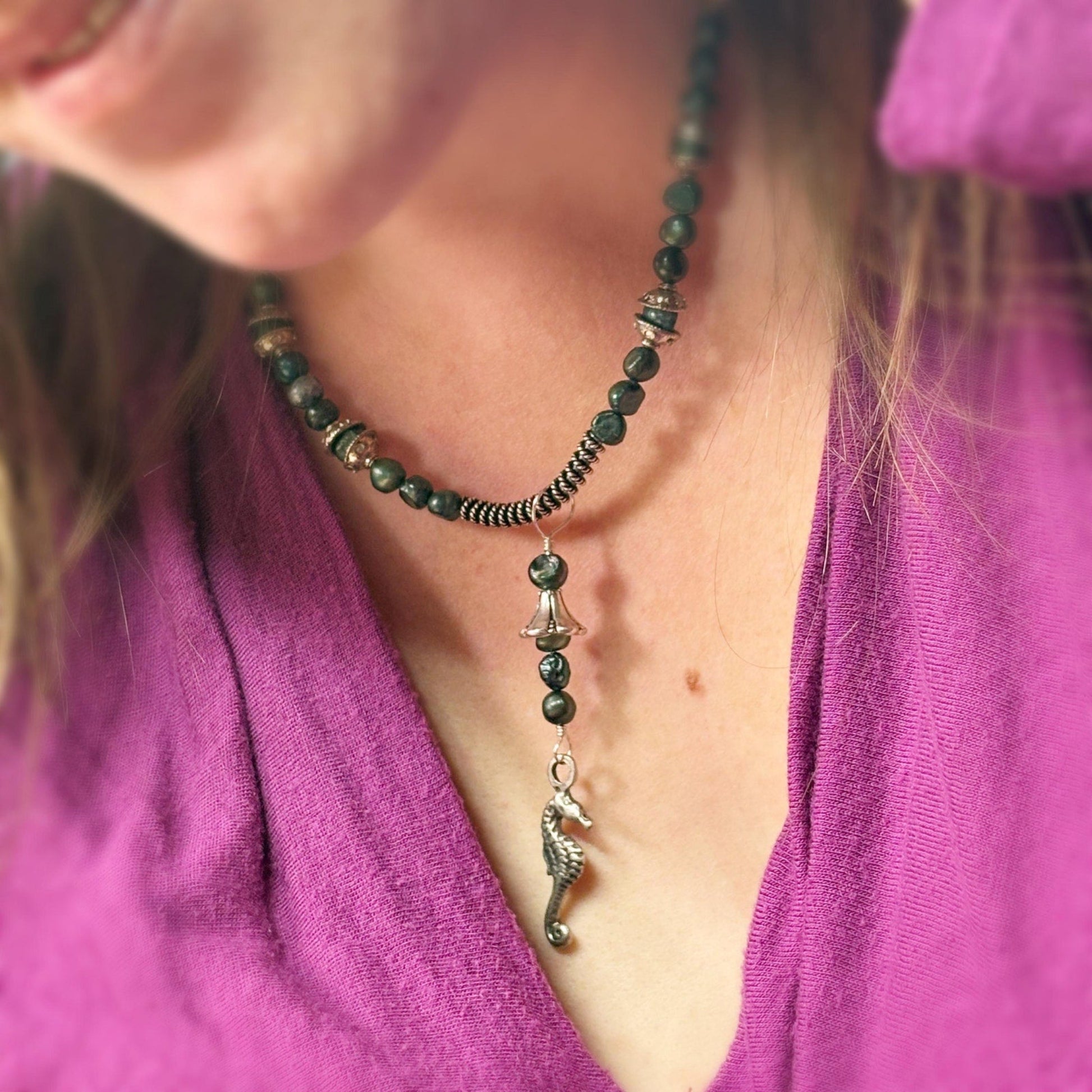 Person wearing a necklace with a seahorse pendant, close-up on a purple shirt.