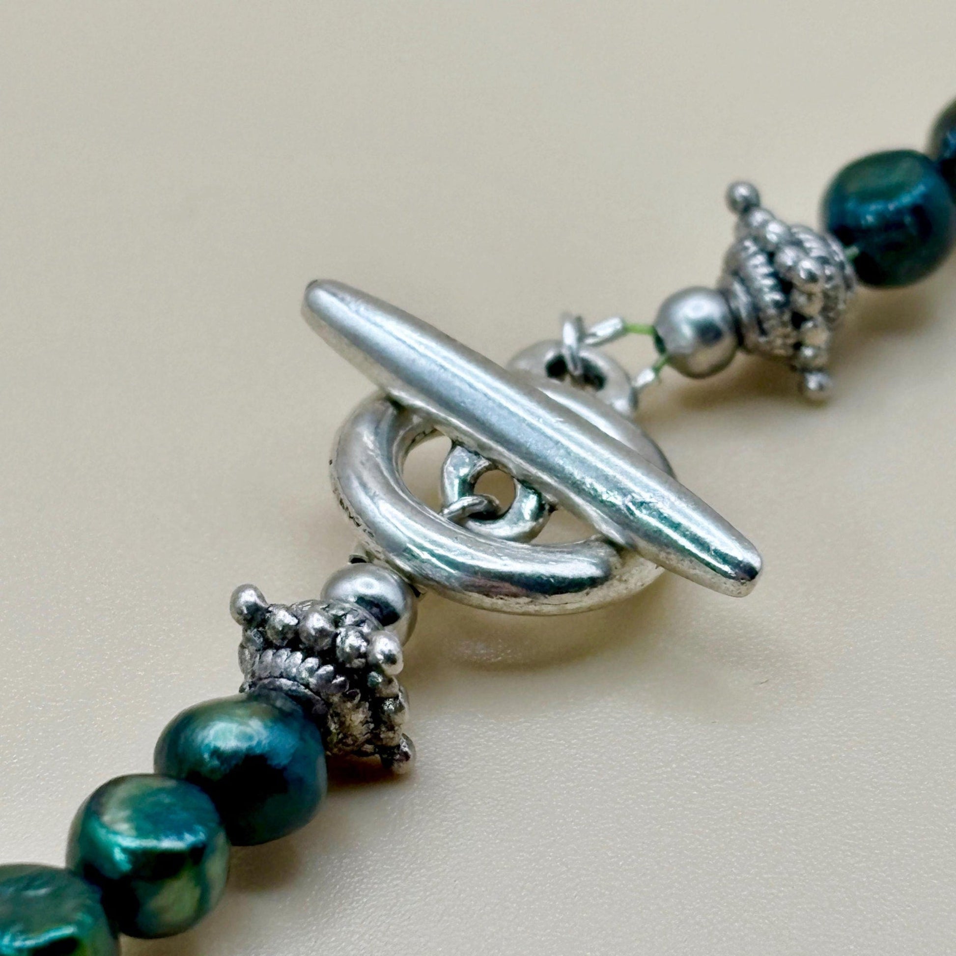 Close-up of a necklace with green beads and silver clasp on a beige background