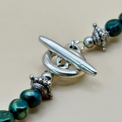 Close-up of a necklace with green beads and silver clasp on a beige background