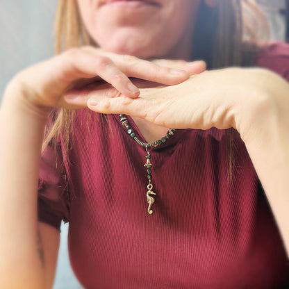 Person wearing a maroon top with a necklace featuring a seahorse pendant.