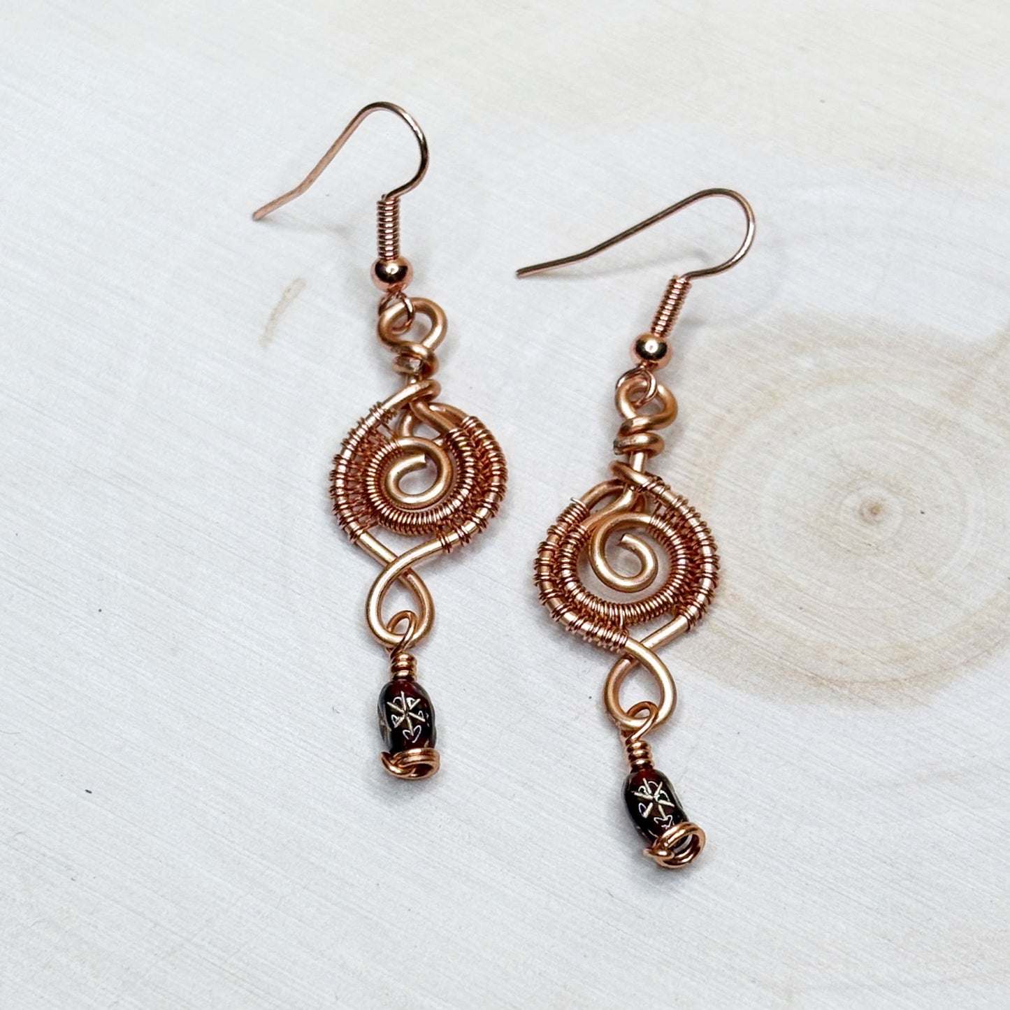Copper wire-wrapped earrings with decorative beads on a light background