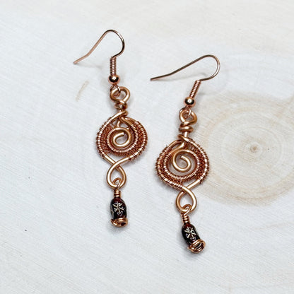 Copper wire-wrapped earrings with decorative beads on a light background