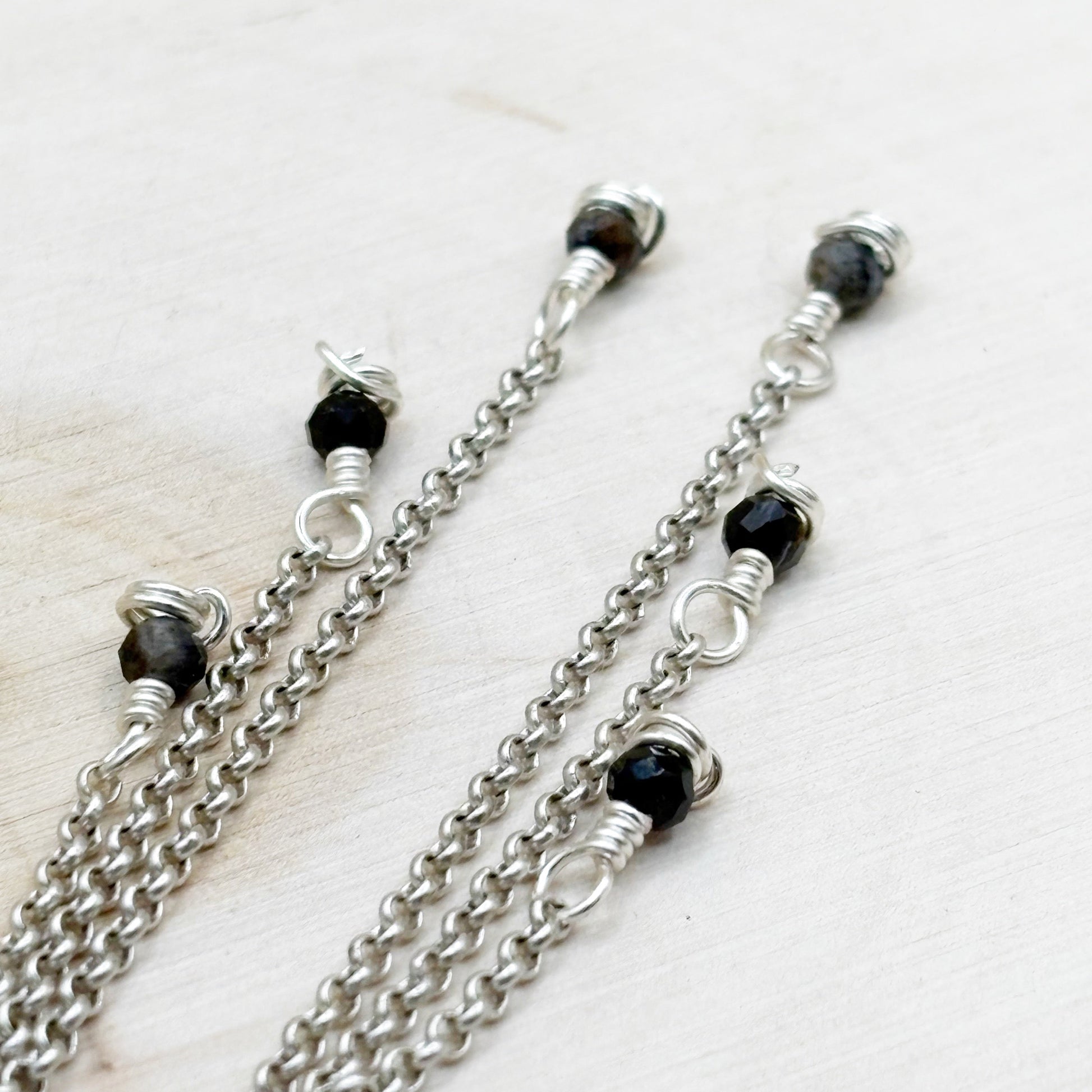 Silver chains with black beads on a light wooden surface