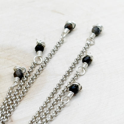 Silver chains with black beads on a light wooden surface