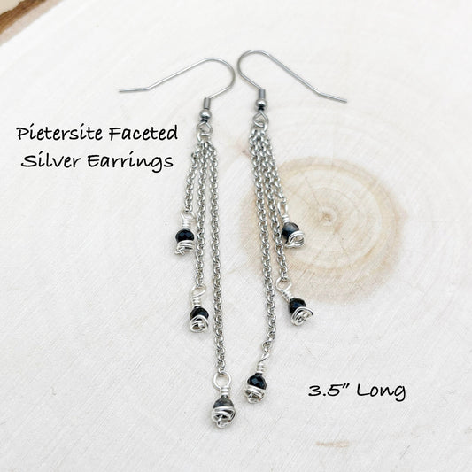 Chain style earrings sitting on a wood background with dark blue shiny stones