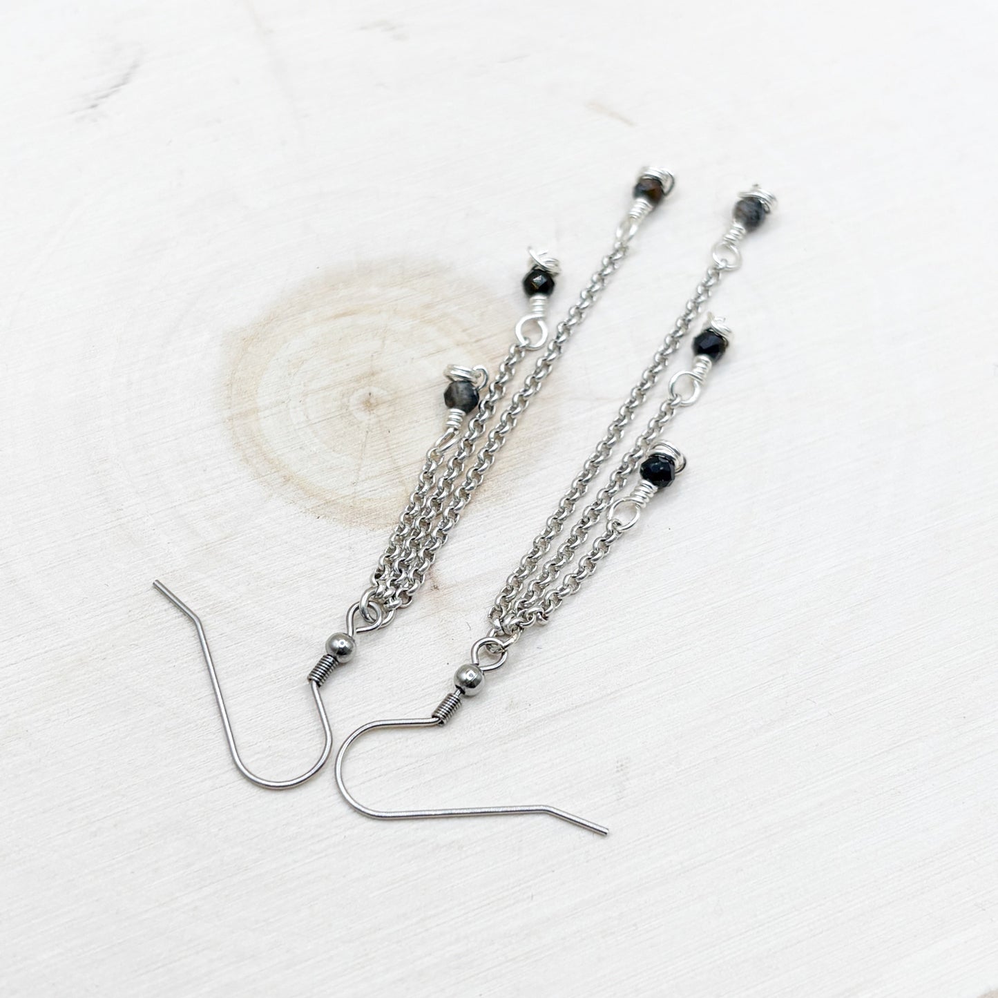 Silver chain earrings with dark blue shiny beads on a white background