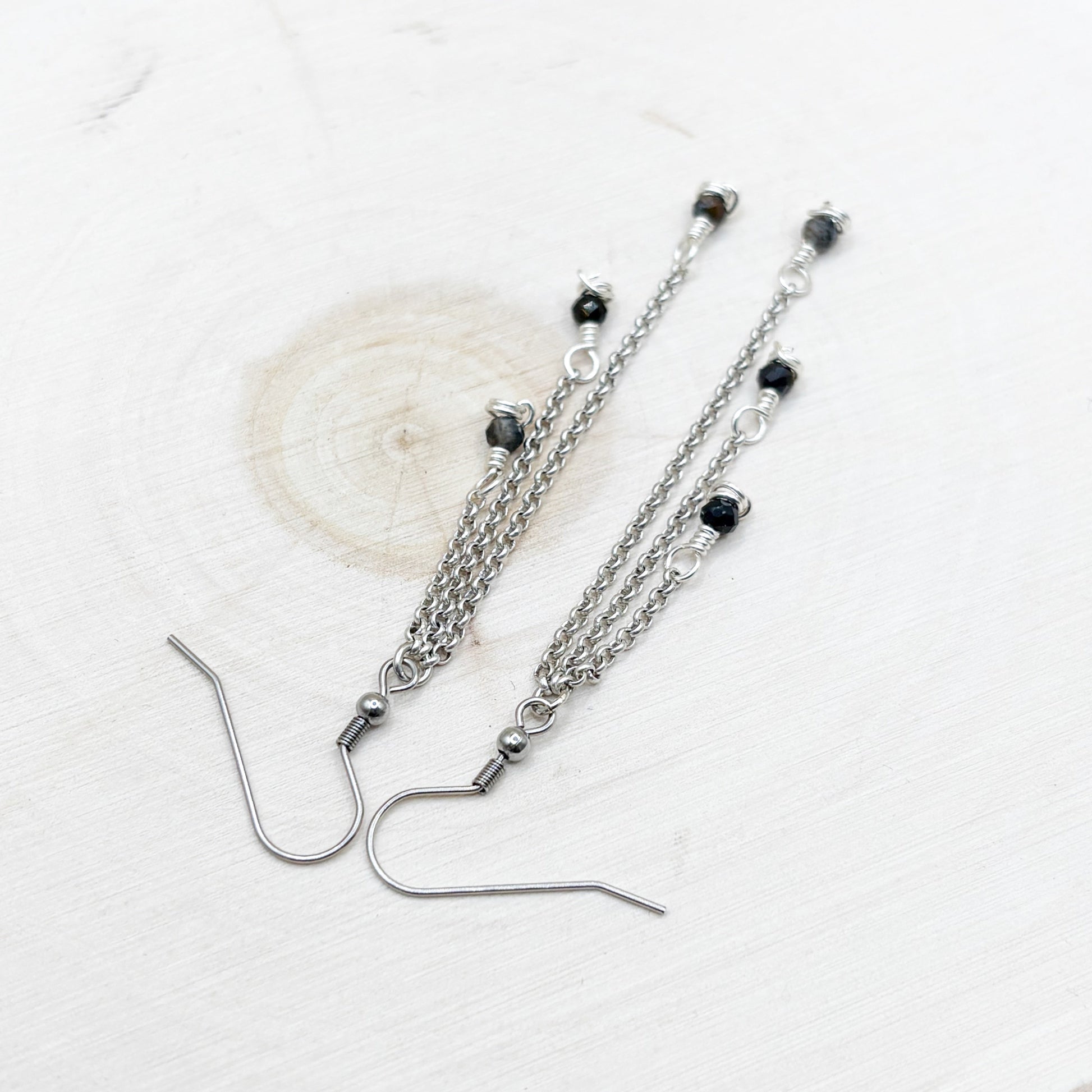 Silver chain earrings with dark blue shiny beads on a white background