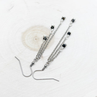 Silver chain earrings with dark blue shiny beads on a white background