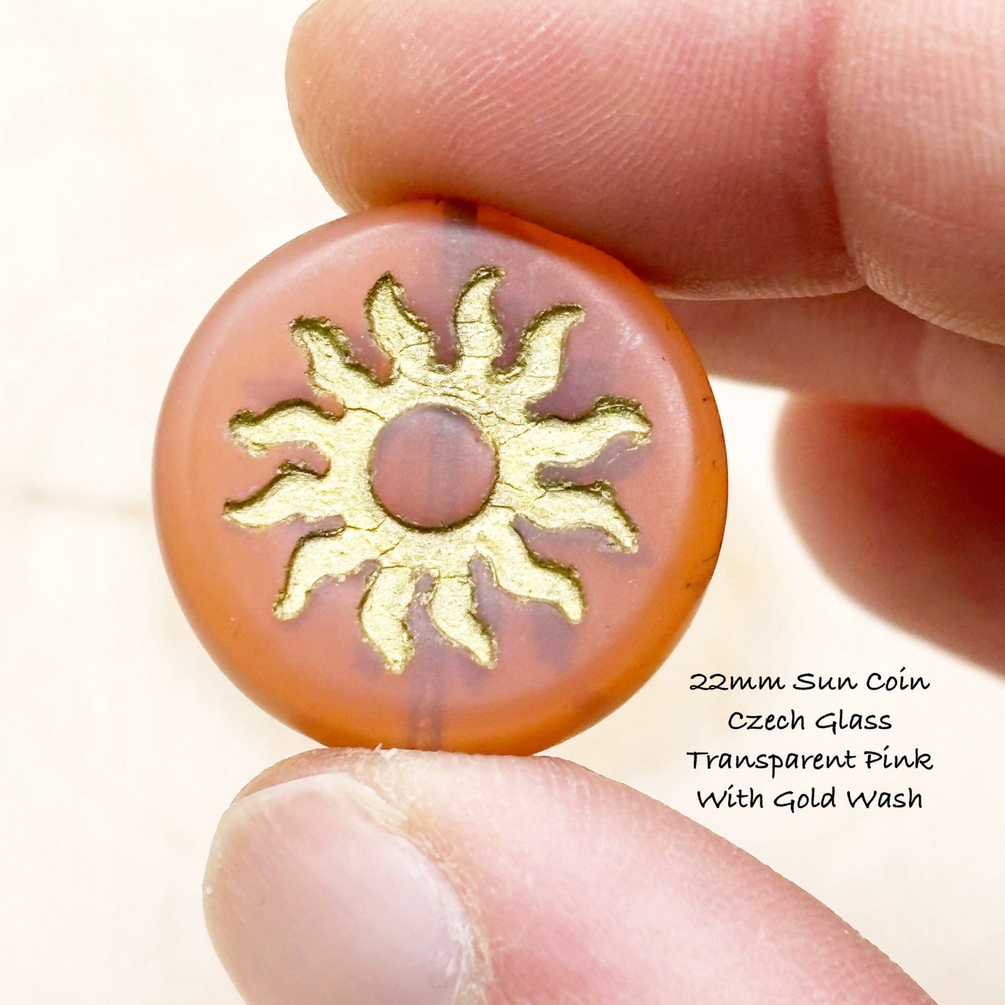Round Czech glass coin with gold sun design held between fingers on a light background