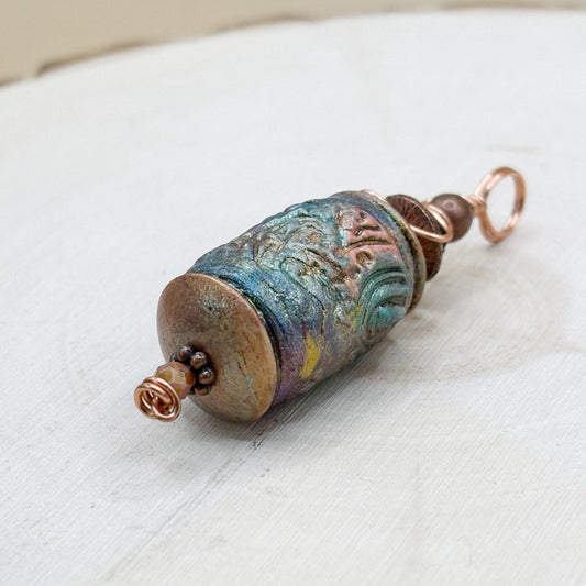 Decorative metal pendant with textured surface on a white wood background